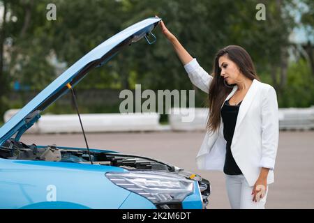 Frau Fahrer im eleganten Anzug untersucht gebrochene Motorhaube Stockfoto