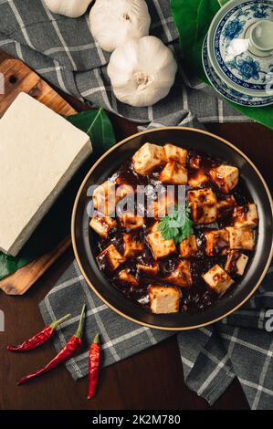 Traditionelle scharfe chinesische Gerichte, Mapo Tofu mit Teetasse, auf Holzplatte mit dunklem Hintergrund. Stockfoto