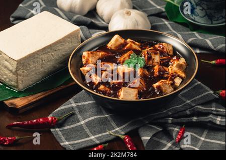 Traditionelle scharfe chinesische Gerichte, Mapo Tofu mit Teetasse, auf Holzplatte mit dunklem Hintergrund. Stockfoto