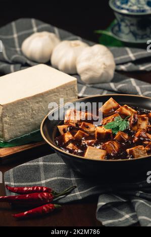 Traditionelle scharfe chinesische Gerichte, Mapo Tofu mit Teetasse, auf Holzplatte mit dunklem Hintergrund. Stockfoto