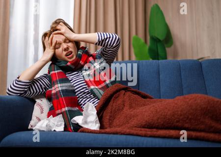 Junge Frau, die an einem Grippevirus erkrankt ist und unter starken Kopfschmerzen leidet, während sie auf der Couch liegt Stockfoto