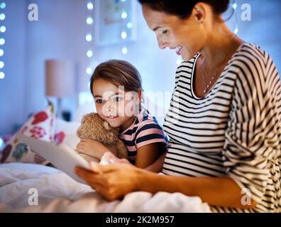 In eine interaktive Geschichte vertieft. Eine kurze Aufnahme einer attraktiven jungen Schwangeren, die ihre Tochter auf einem Tablet mit einer Geschichte zur Schlafenszeit vorliest. Stockfoto