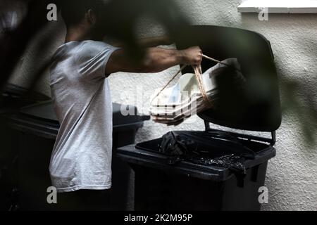 Recycling ist eine tägliche Wahl. Aufnahme eines jungen Mannes, der Zeitung in den Papierkorb legte, um recycelt zu werden. Stockfoto