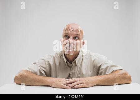 Rücksichtsvoller, älterer, kahlköpfiger Mann, der an einem Tisch sitzt Stockfoto