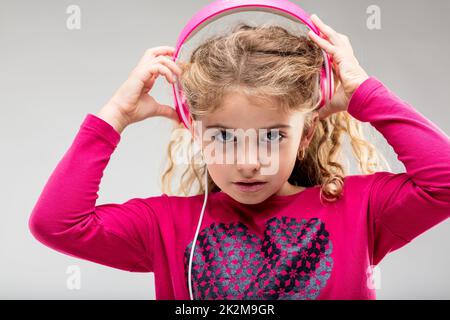 L Girl hört Musik auf pinkfarbenen Kopfhörern Stockfoto