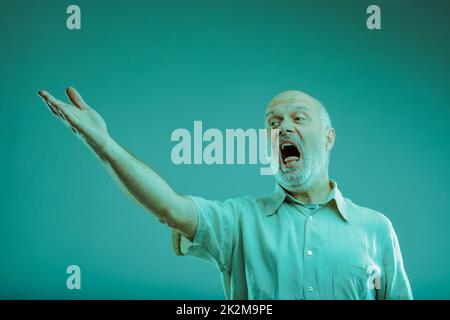 Ein älterer Mann, der singt oder jemanden anschreit, der mit der Hand Gesten macht Stockfoto