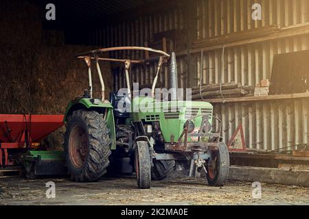 Keine Farm ist komplett ohne eine. Aufnahme eines rostigen alten Traktors, der in einer leeren Scheune steht. Stockfoto