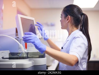 Unterstützung der wissenschaftlichen Forschung mit modernsten Geräten. Aufnahme eines jungen Wissenschaftlers, der einen Computer benutzt, um einen medizinischen Test in einem Labor durchzuführen. Stockfoto