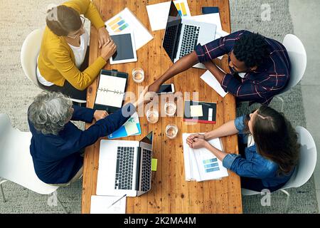 Vielen Dank, dass Sie sich heute Zeit genommen haben. Ein Team von Kreativen, die sich gegenseitig die Hände über einen Tisch schüttelten, hat eine Aufnahme in einem hohen Winkel gemacht. Stockfoto