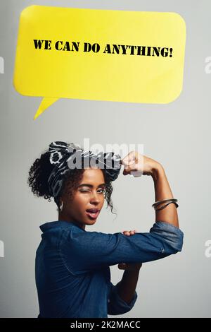 Eine Frau zu sein, hat Stärke. Studiofoto einer attraktiven jungen Frau, die posiert, mit einer Sprechblase, die "Wir können alles vor grauem Hintergrund" liest. Stockfoto