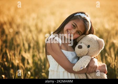 Finden Sie die Sonne in jedem Tag. Porträt eines niedlichen kleinen Mädchens, das mit ihrem Teddybären auf einem Kornfeld spielt. Stockfoto