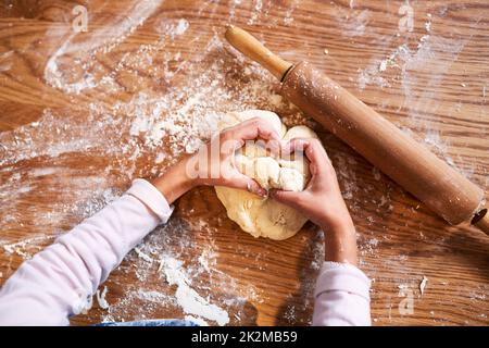 Rollen und Falten. Ein kleines Mädchen knetet Teig, während es zu Hause bäckt. Stockfoto