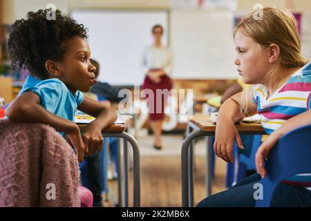 Mobbing muss genau überwacht werden. Aufnahme eines jungen Mädchens, das in der Schule im Klassenzimmer sitzt und ihre Zunge an ihrem Klassenkameraden herauszieht. Stockfoto