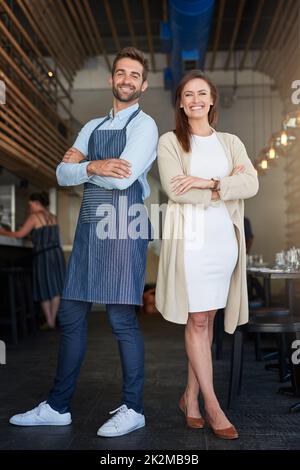Führen ihr Geschäftsreich zusammen. Porträt zweier junger Unternehmer, die in ihrem Café stehen. Stockfoto