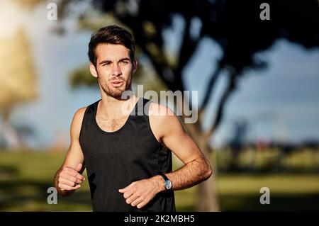 Machen Sie einfach weiter. Aufnahme eines jungen Mannes, der in einem Park joggt. Stockfoto