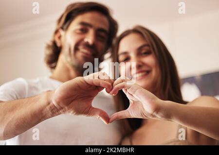 Herzen lässt die Liebe wachsen. Aufnahme eines jungen Paares, das mit den Händen zu Hause ein Herzzeichen macht. Stockfoto