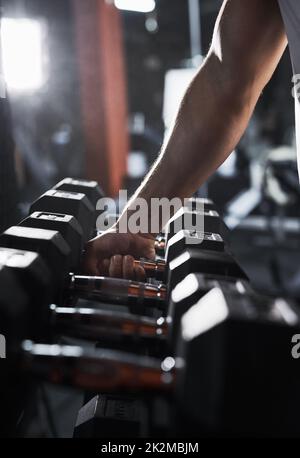 Nehmen wir ein schwereres Gewicht. Kurzer Schuss eines nicht erkennbaren männlichen Athleten, der während seines Trainings im Fitnessstudio eine Reihe von Hanteln ergriff. Stockfoto