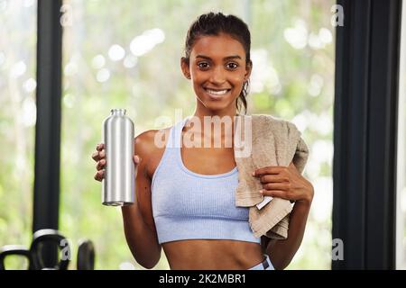 Meine Gesundheit ist meine oberste Priorität. Aufnahme einer schönen jungen Frau, die ihre Wasserflasche und ihr Handtuch im Fitnessstudio hält. Stockfoto