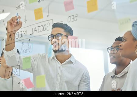 Eine erfolgreiche Strategie entwickeln. Eine kurze Aufnahme einer Gruppe verschiedener junger Geschäftsleute, die im Sitzungssaal an einem Glaswischbrett arbeiten. Stockfoto