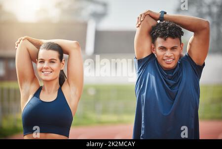 Aufwärmen für den Sieg. Beschnittenes Porträt von zwei jungen Athleten, die sich aufwärmen und dabei auf der Strecke aufstehen. Stockfoto