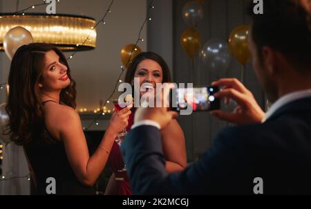 Den Moment festhalten. Ausgeschnittene Aufnahme eines unkenntlichen Mannes, der ein Foto von zwei attraktiven jungen Frauen in einem Nachtclub macht. Stockfoto