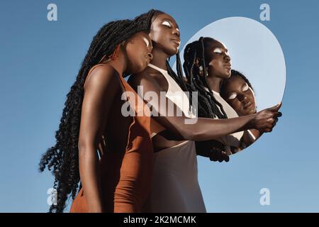 Die Schönheit in mir spiegelt sich auf dich zurück. Aufnahme von zwei attraktiven jungen Frauen, die einen Spiegel mit ihrer Spiegelung vor einem Himmelshintergrund halten. Stockfoto