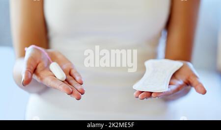 Welches bevorzugen Sie? Ausgeschnittene Aufnahme einer nicht erkennbaren Frau, die einen Tampon und ein Pad in ihren Händen hält. Stockfoto