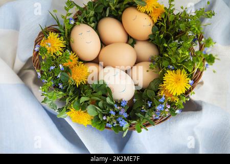 Wunderschönes Frühlingsbouquet in einem Holzkorb mit Osterbemalung, Eiern mit süßen Gesichtern. Stockfoto