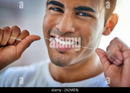 Mein Lächeln verlangt, dass ich das tue. Porträt eines glücklichen jungen Mannes, der zu Hause seine Zähne mit Zahnseide verputzt. Stockfoto