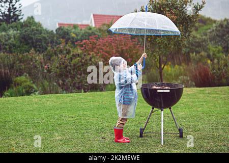 Das Fleisch muss trocken bleiben. Ganzkörperaufnahme eines Jungen, der im Regen vor einem Grill im Freien steht. Stockfoto