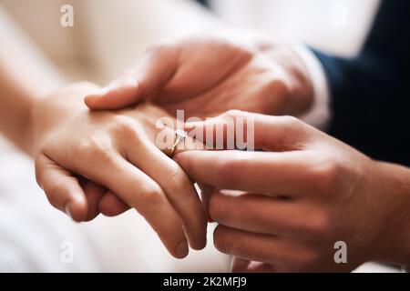 Kein Diamant kann mit dieser kostbaren Liebe vergleichen. Ausgeschnittene Aufnahme eines unkenntlichen Bräutigams, der während der Hochzeit einen Diamantring auf den Finger seiner Frau legt. Stockfoto