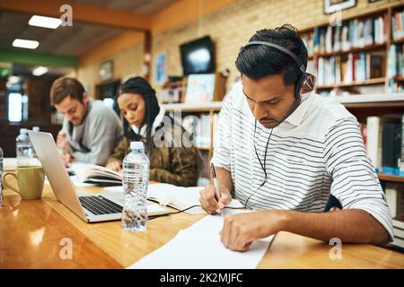 HES konzentrierte sich auf seine Studien. Eine Aufnahme eines jungen Studenten der Universität, der in der Bibliothek mit anderen Studenten im Hintergrund studiert. Stockfoto