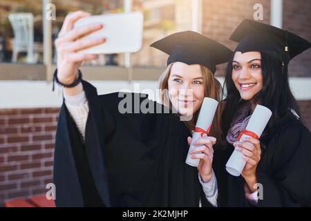 Jeder zu Hause wartet auf dieses Selfie. Zugeschnittene Aufnahme von zwei Studenten, die am Abschlusstag ein Selfie machen. Stockfoto