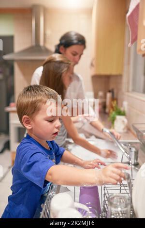 Viele Hände bei der Arbeit. Aufnahme eines kleinen Jungen, der mit seiner Familie an einem Spülbecken abspült. Stockfoto