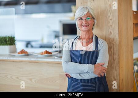 Vergessen Sie Stricken, ich habe ein Geschäft zu laufen. Porträt einer selbstbewussten älteren Geschäftsbesitzerin, die mit einer Schürze in ihrem Café posiert. Stockfoto