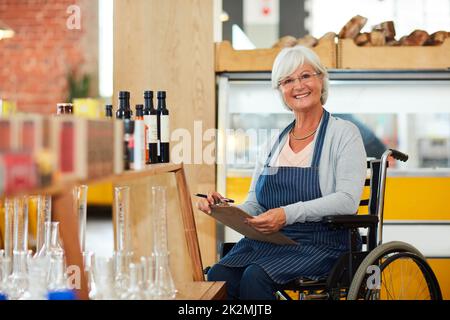 Ich bleibe auf meinem Vorrat. Porträt einer älteren Frau im Rollstuhl, die in ihrem Café eine Bestandsaufnahme macht. Stockfoto