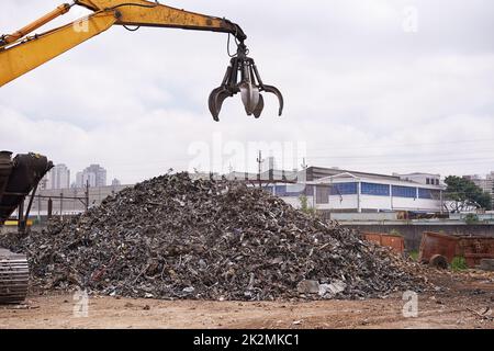 Im Geschäft mit Metall. Ausgeschnittene Aufnahme eines Baggers, der durch einen Haufen von Metallschrott sortiert. Stockfoto