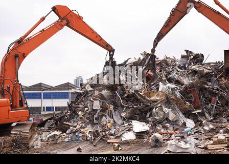 Industrielle Neuverwendung. Ausgeschnittene Aufnahme von zwei Baggern, die durch einen Haufen von Metallschrott sortieren. Stockfoto