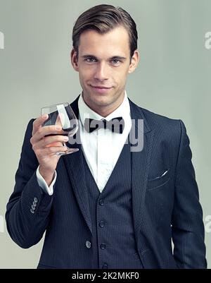 Heres to Frivolity. Ein Porträt eines eleganten jungen Mannes mit einem Glas Wein in einem Vintage-Anzug. Stockfoto