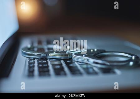 Treffen Sie zusätzliche Vorsichtsmaßnahmen, um sich vor Cyberkriminalität zu schützen. Aufnahme eines Paares Handschellen, die im Dunkeln auf einer Laptop-Tastatur liegen. Stockfoto