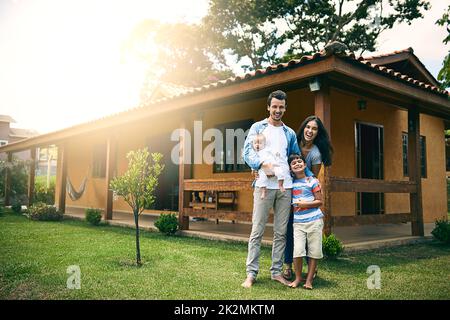 Wir sind eine glückliche Familie. Ganzkörperportrait einer glücklichen, jungen vierköpfigen Familie draußen mit ihrem Haus im Hintergrund. Stockfoto