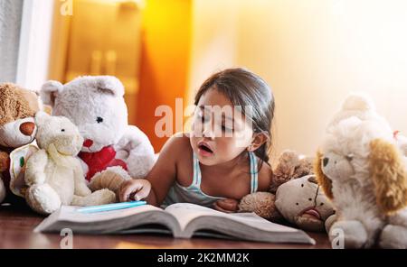 Das Buch hat ihre volle Aufmerksamkeit. Aufnahme eines fokussierten kleinen Mädchens, das tagsüber in einem Buch auf dem Boden zu Hause lag.
