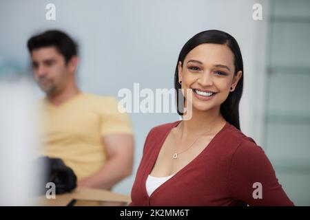 Mit dem Vertrauen bleiben Sie stets im Vordergrund Ihres Geschäftsspiels. Foto einer selbstbewussten jungen Geschäftsfrau, die in einem modernen Büro mit ihrem Kollegen im Hintergrund arbeitet. Stockfoto