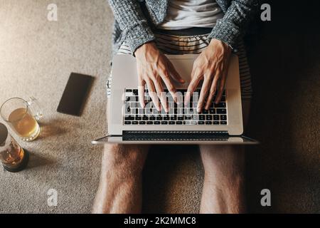 Nicht abgezapftes WLAN bedeutet grenzenloses Surfen. High-Angle-Aufnahme eines unkenntlichen Mannes, der seinen Laptop benutzt, während er zu Hause auf dem Boden sitzt. Stockfoto