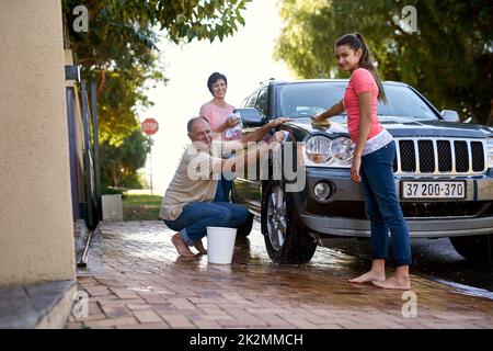 Bindungszeit für die Familie. Porträt einer Familie, die draußen ein Auto gemeinsam wäscht. Stockfoto