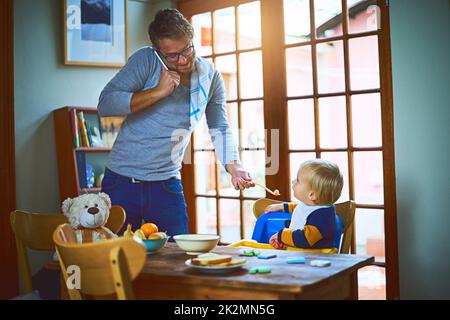 DVDAD weiß, wie man Multitasking. Ausgeschnittene Aufnahme eines alleinerziehenden Vaters auf einem Anruf, während er seinen Sohn zu Hause fütterte. Stockfoto