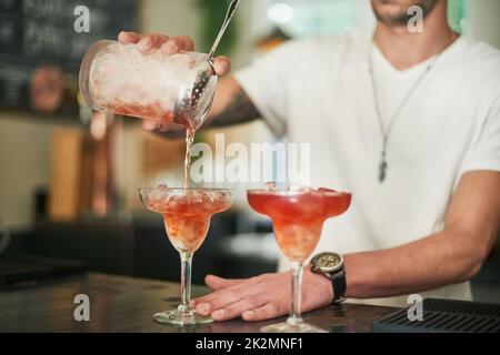 Durstig. Ein kurzer Schuss eines nicht identifizierbaren Barkeepers, der einen Cocktail hinter die Bar ausschüttet. Stockfoto