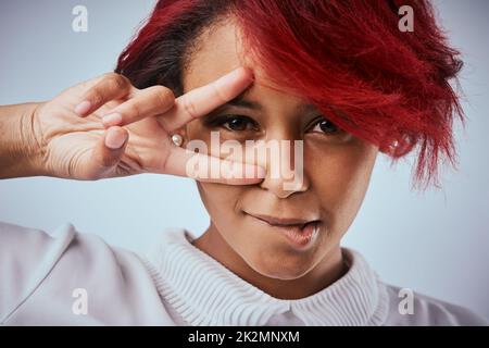 Habt keine Angst, euch selbst zu sein. Studioaufnahme einer schönen jungen Frau, die die Friedensgeste über ihrem Auge zeigt. Stockfoto