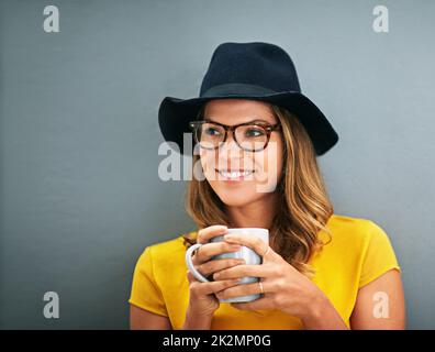 Shes hat einen eigenen Kopf. Aufnahme einer jungen Frau, die vor grauem Hintergrund Kaffee trinkt. Stockfoto