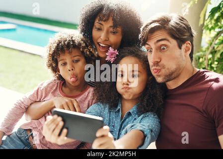 Die F in Familie steht für Spaß. Aufnahme einer schönen jungen Familie, die im Freien ein Selfie zusammen gemacht hat. Stockfoto